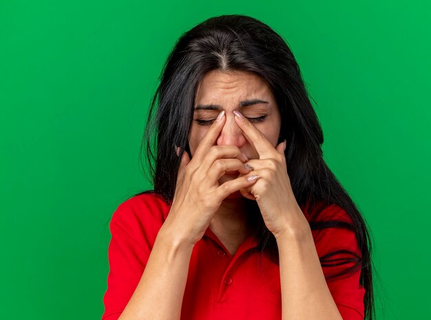 Close-up beeld van pijnlijke jonge zieke vrouw vingers op neus zetten met gesloten ogen geïsoleerd op groene muur met kopie ruimte