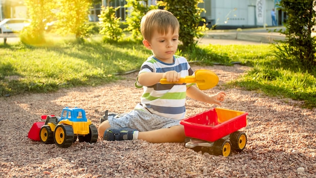 Close-up beeld van schattige kleine jongen spelen op de palyground met speelgoed. kind plezier met vrachtwagen, graafmachine en aanhanger