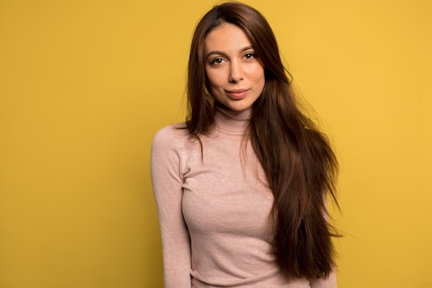 Gratis foto close-up binnen portret van mooi mooi meisje met lang donker haar roze shirt dragen poseren over gele muur