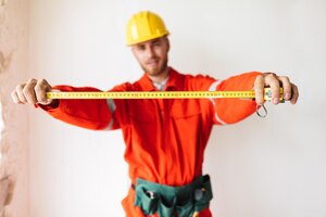 Close-up bouwer in oranje werkkleding en gele veiligheidshelm met meetlint op witte achtergrond