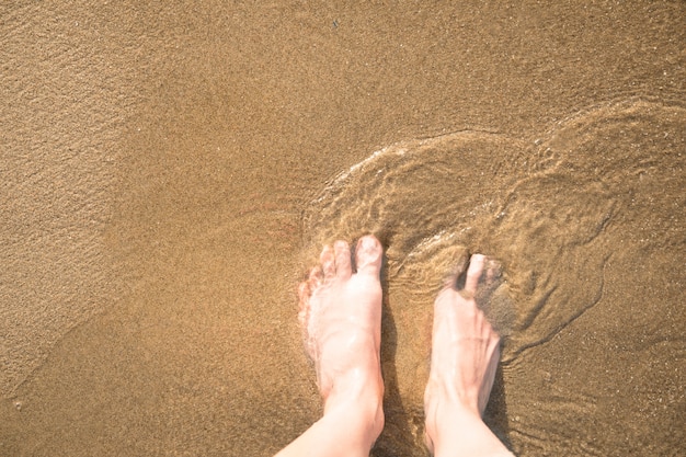 Gratis foto close-up bovenaanzicht van de voeten in nat zand