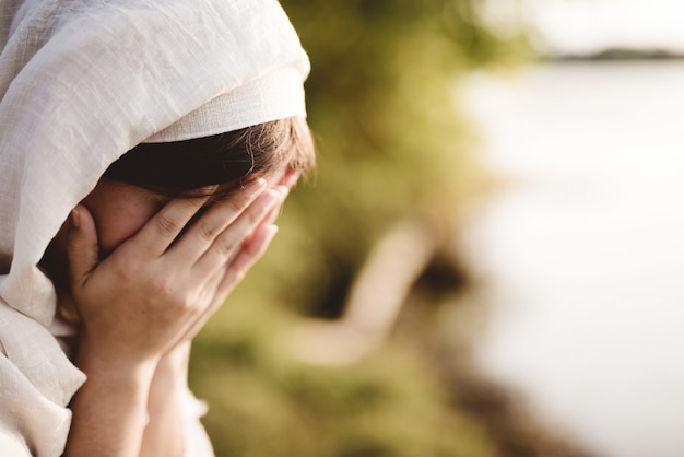 Gratis foto close-up die van een wijfje is ontsproten dat een bijbelse robe draagt die met een vage achtergrond bidt