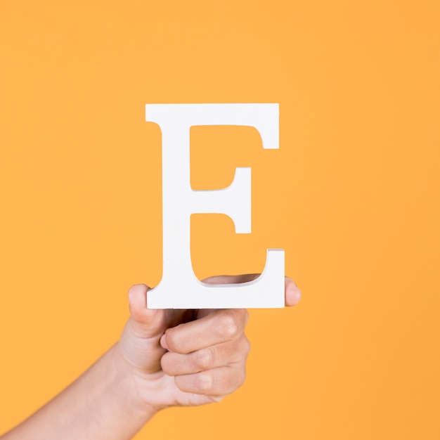 Close-up die van hand de hoofdletter e in hoofdletters over gele achtergrond steunen
