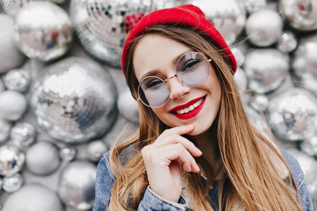 Close-up foto van blij meisje met lichte make-up poseren in de buurt van discoballen. portret van charmante witte jonge vrouw in casual kleding glimlachen