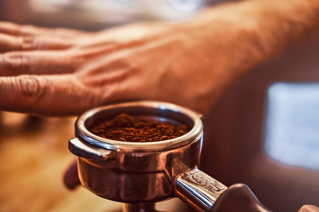 Close-up foto van een barista-hand die een portafilter vasthoudt met een zwarte gemalen koffie in een café-winkel of restaurant