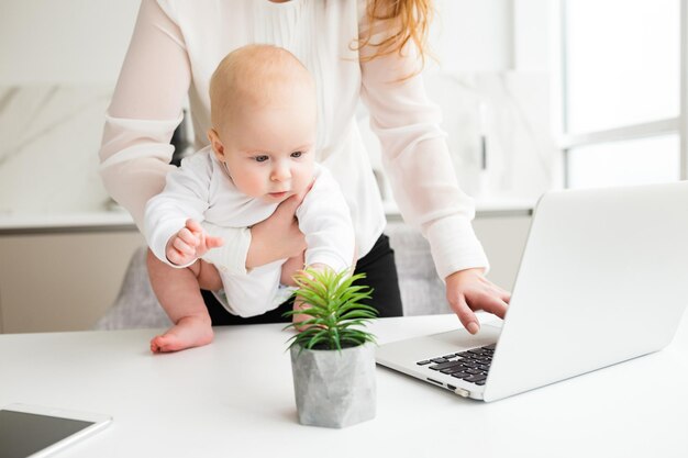 Close-up foto van kleine baby in de hand die dromerig naar de plant kijkt terwijl zijn moeder op laptop werkt