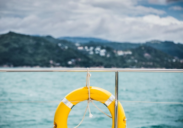 Close-up gele reddingsring die op boot met oceaanachtergrond hangt.