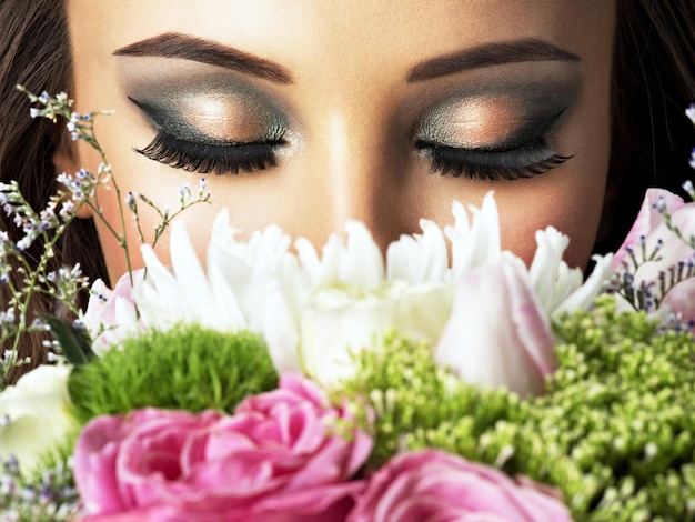 Gratis foto close-up gezicht van mooi meisje met bloemen. jonge aantrekkelijke vrouw houdt het boeket van lentebloemen