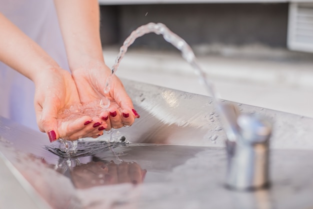 Close-up op vrouwelijke hand die water opvangt. Spatten druppels op zonnige zomer buitenshuis achtergrond. Milieu en gezondheid concept. Flowing Fountain Cool Drink