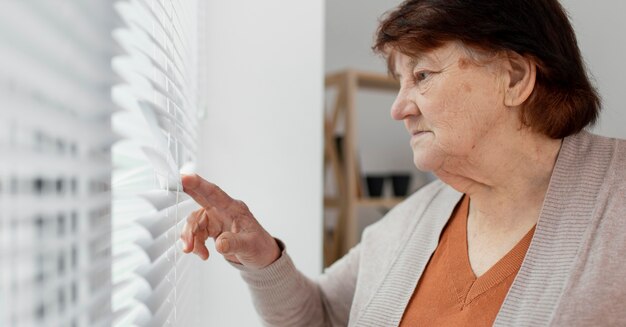 Close-up oude vrouw kijkt uit het raam