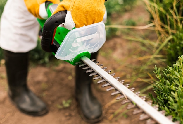 Gratis foto close-up persoon met behulp van trimmen tool op bush