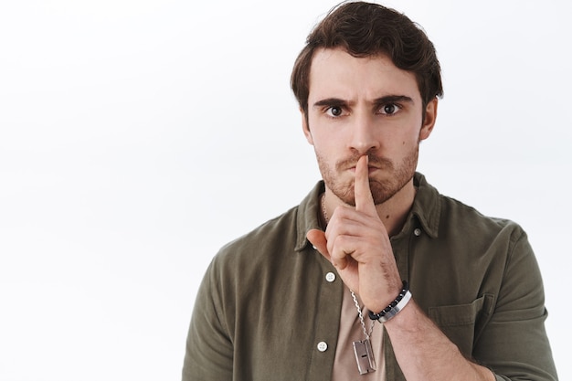 Close-up portret boze, bazige knappe kerel die zegt: blijf stil, vraag stilte, zwijg met de vinger tegen de lip gedrukt