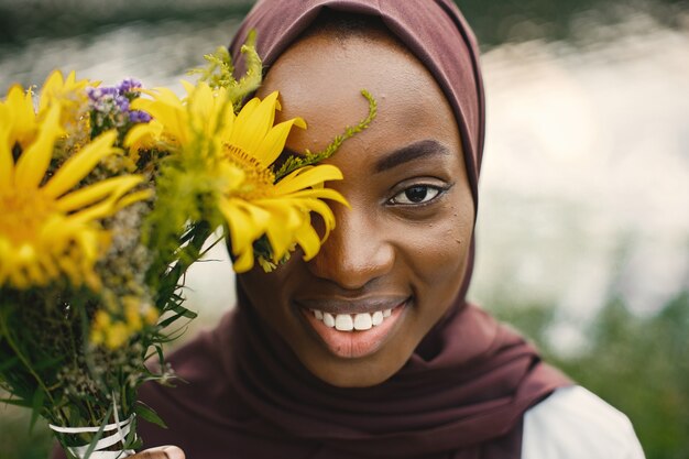 Close-up portret glimlachende moslimvrouw die de helft van het gezicht bedekt met gele bloemen