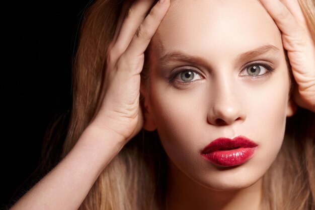 Close-up portret van blonde vrouw met rode lippen geïsoleerd op zwarte achtergrond.