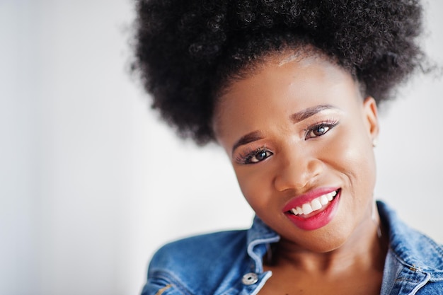 Close-up portret van een aantrekkelijke Afro-Amerikaanse vrouw met afro-haar en jeansjasje geposeerd in witte kamer Modieus zwart model