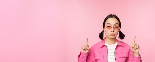 Close-up portret van een Aziatisch stijlvol meisje dat sceptisch kijkt met een wijzende vinger omhoog met een ongeamuseerd gezicht dat over een roze achtergrond staat