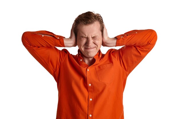 Close-up portret van een jonge atletische gemberpeson in een stijlvol oranje shirt die doet alsof hij geen geluiden wil horen terwijl hij poseert geïsoleerd op een witte studioachtergrond. Menselijke gezichtsuitdrukkingen.