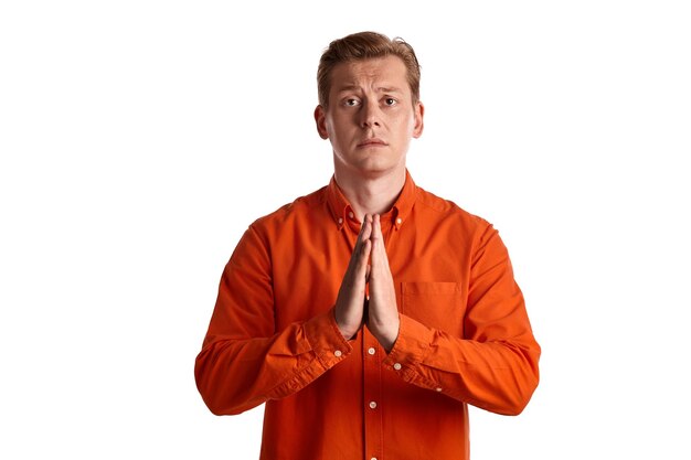 Close-up portret van een jonge, elegante gemberman in een stijlvol oranje shirt die doet alsof hij bidt en naar de camera kijkt terwijl hij zich voordeed op een witte studioachtergrond. Menselijke gezichtsuitdrukkingen. Sinc