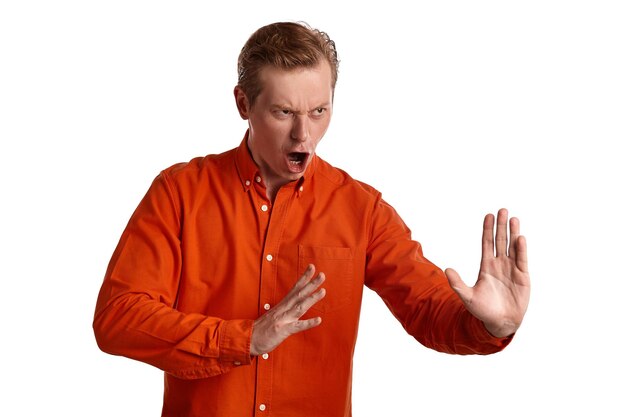 Close-up portret van een jonge goed gember peson in een stijlvol oranje shirt doet alsof hij vecht terwijl hij poseert geïsoleerd op een witte studio achtergrond. Menselijke gezichtsuitdrukkingen. Oprechte emoties houden verband met