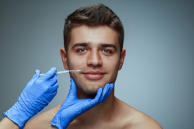 Close-up portret van een jonge man geïsoleerd op grijze studio achtergrond. operatieprocedure vullen. concept van de gezondheid en schoonheid van mannen, cosmetologie, zelfzorg, lichaams- en huidverzorging. anti-veroudering.