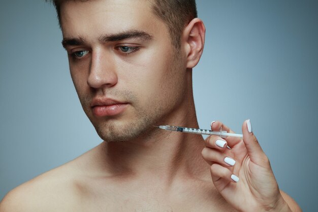 Close-up portret van een jonge man geïsoleerd op grijze studio achtergrond. Operatieprocedure vullen. Concept van de gezondheid en schoonheid van mannen, cosmetologie, zelfzorg, lichaams- en huidverzorging. Anti-veroudering.