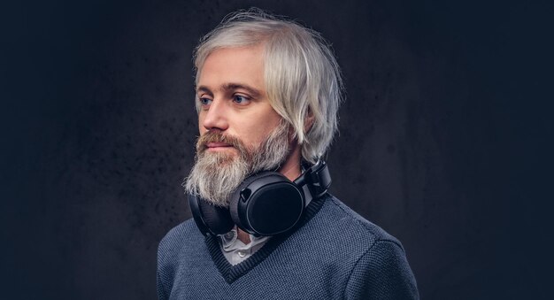 Close-up portret van een knappe senior man die naar muziek luistert in een koptelefoon. Geïsoleerd een donkere achtergrond.