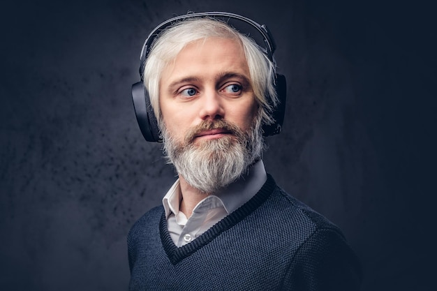 Close-up portret van een knappe senior man die naar muziek luistert in een koptelefoon. Geïsoleerd een donkere achtergrond.