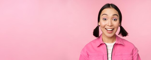 Close-up portret van een mooi Aziatisch meisje dat er enthousiast uitziet en lacht, lacht en glimlacht, gelukkig staat tegen een roze achtergrond