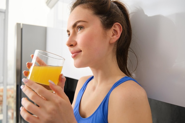 Gratis foto close-up portret van een mooie jonge vrouw die wegkijkt en fris sinaasappelsap in een glas drinkt