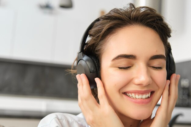 Close-up portret van een schattige jonge vrouw die glimlacht en naar muziek luistert in draadloze koptelefoon