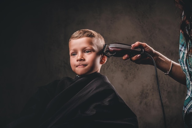 Close-up portret van een schattige kleuterjongen die kapsel krijgt op een donkere achtergrond.