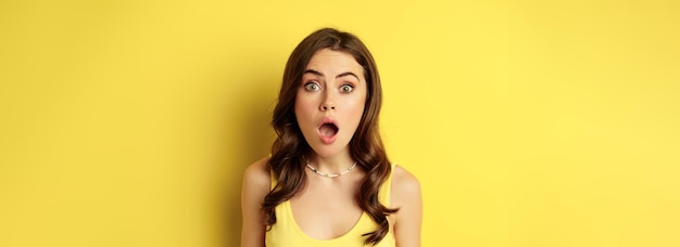Close-up portret van een stijlvol brunette meisje dat een verbaasd wow-gezicht kijkt met opwinding en verrassing onder de indruk van iets dat over een gele achtergrond staat