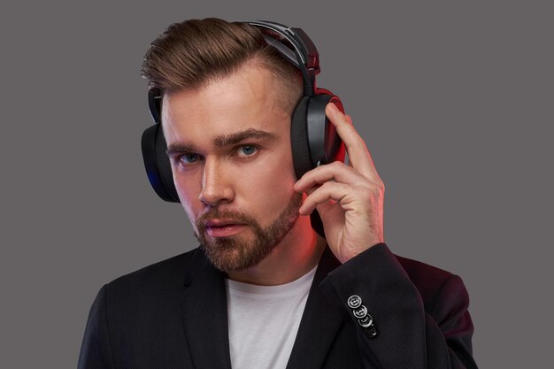 Close-up portret van een stijlvolle bebaarde man met kapsel luisteren naar muziek in koptelefoon. Geïsoleerd op een grijze achtergrond.