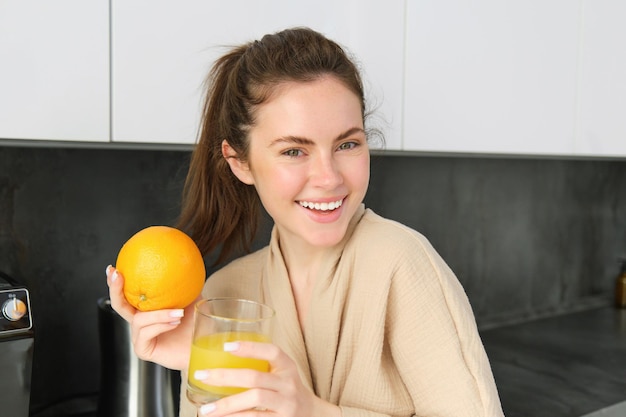 Gratis foto close-up portret van een stijlvolle moderne vrouw die vers sap drinkt uit een glas in de keuken met een