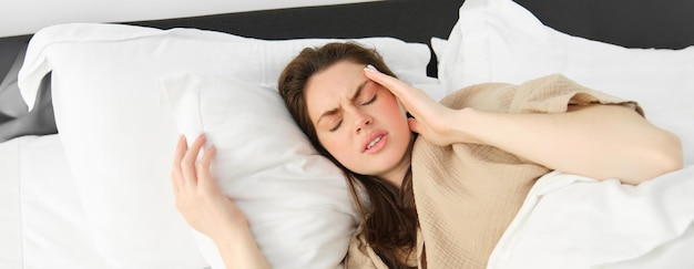 Gratis foto close-up portret van een zieke vrouw die in haar bed ligt en zich onwel voelt door haar hoofd aan te raken, heeft hoofdpijn