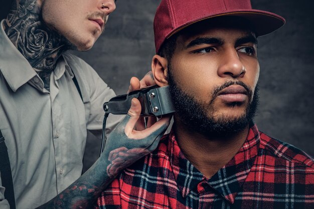 Close-up portret van getatoeëerde mannelijke kapper bezuinigingen, baard aan een zwarte man.