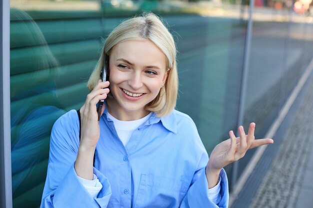 Gratis foto close-up portret van glimlachende blonde vrouw chatten aan de telefoon praten op mobiele telefoon staande