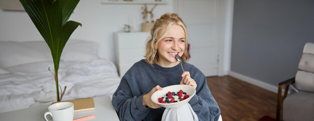 Close-up portret van glimlachende schattige blonde vrouw die een gezonde lunch eet in haar kamer met een schaal in haar hand.