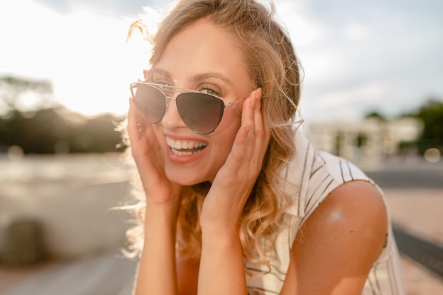 Close-up portret van jonge aantrekkelijke stijlvolle blonde vrouw in stad straat in zomer mode stijl jurk zonnebril te houden