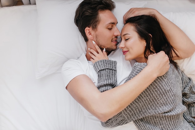 Close-up portret van knappe jongen omhelst zachtjes zwartharige vrouw die naast slapen