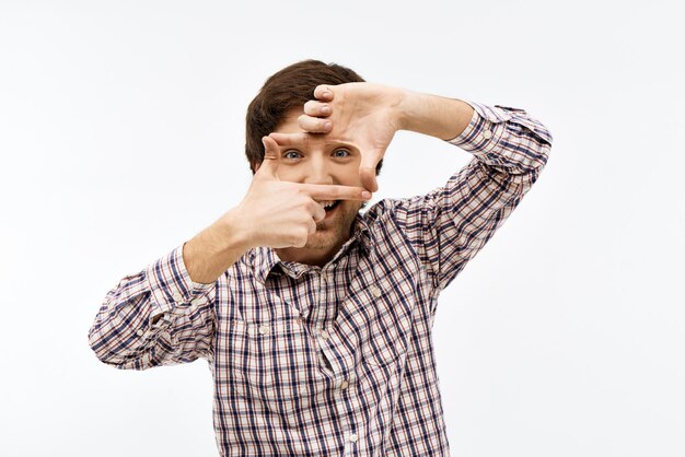 Close-up portret van knappe zelfverzekerde jonge blauwogige donkerharige man met een casual geruit hemd die naar de voorkant kijkt en een frame maakt met zijn handen