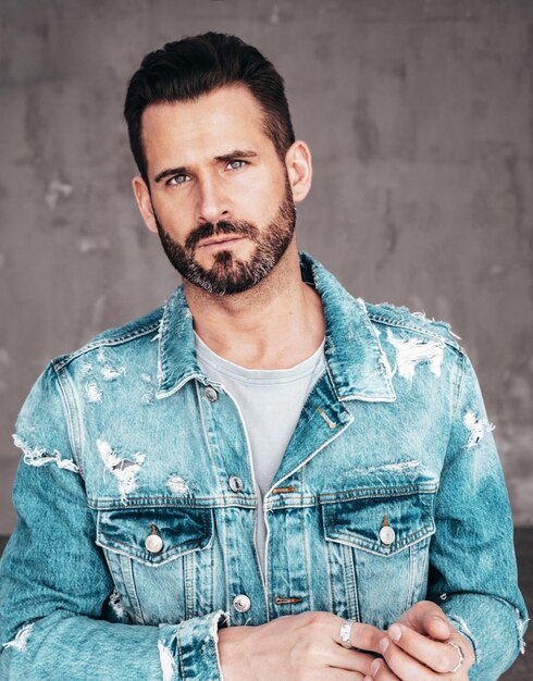 Close-up portret van knappe zelfverzekerde stijlvolle hipster lamberseksueel model Sexy man gekleed in jeans jasje Mode man poseren op grijze achtergrond in studio