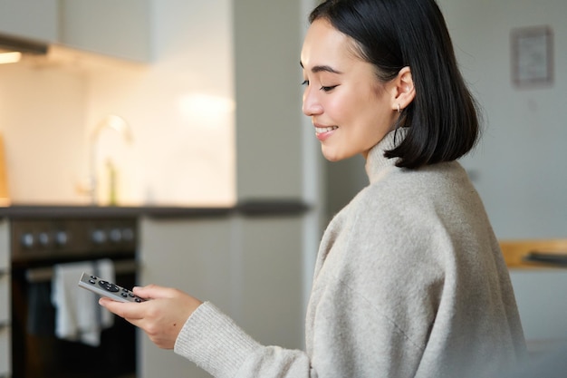 Close-up portret van lachende Aziatische vrouw televisie kijken zittend op de bank met afstandsbediening en switchi