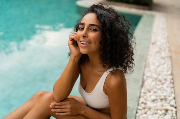 Close-up portret van lachende tann vrouw met krullende haren poseren in zwembad Zomer en vakantie concept