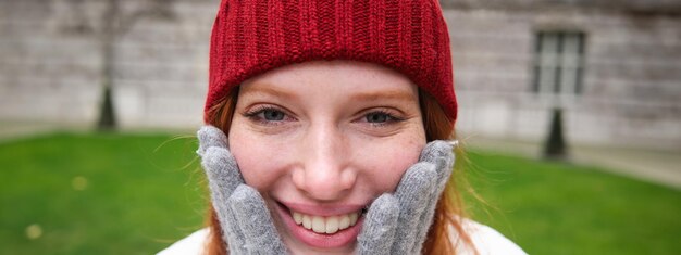 Close-up portret van mooie roodharige vrouw in rode gebreide muts, warme handschoenen glimlachend en kijken