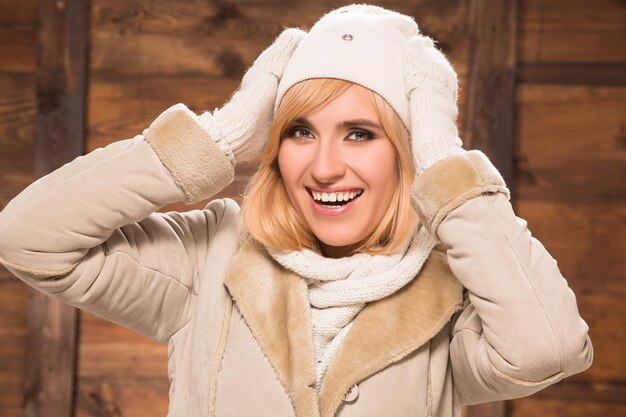 Gratis foto close-up portret van mooie vrouw poseren in hoed, schapenvacht en handschoenen. blondharige dame die haar hoofd aanraakt dat op houten achtergrond wordt geïsoleerd.