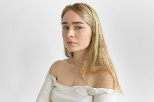 Close-up portret van prachtige jonge vrouw met sluik blond haar, groene ogen en pure huid met sproeten kijken, haar blote schouders laten zien. Natuurlijke schoonheid, vrouwelijkheid, stijl en mode