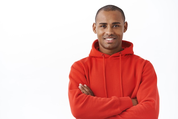 Close-up portret van professionele, succesvolle jonge Afro-Amerikaanse man in rode hoodie, kruis armen borst arms