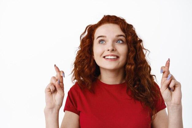 Close-up portret van roodharige hoopvolle vrouw met krullend haar gekruiste vingers voor veel geluk staren naar de linker bovenhoek logo met verleid gezicht wil iets bidden of wensen maken