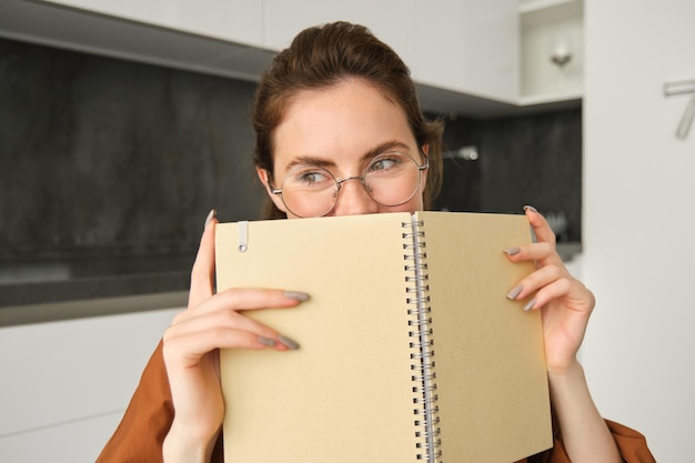 Close-up portret van schattige glimlachende vrouw in een bril die thuis in de keuken zit en haar gezicht achter zich verbergt